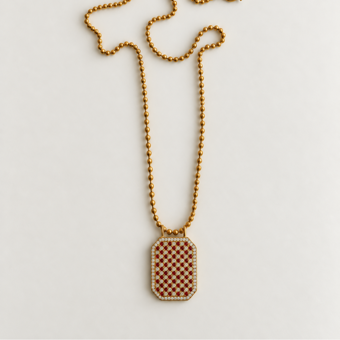 A gold-tone beaded chain necklace with a rectangular pendant featuring a brown and white checkered pattern, bordered with small clear stones, displayed on a light gray background.