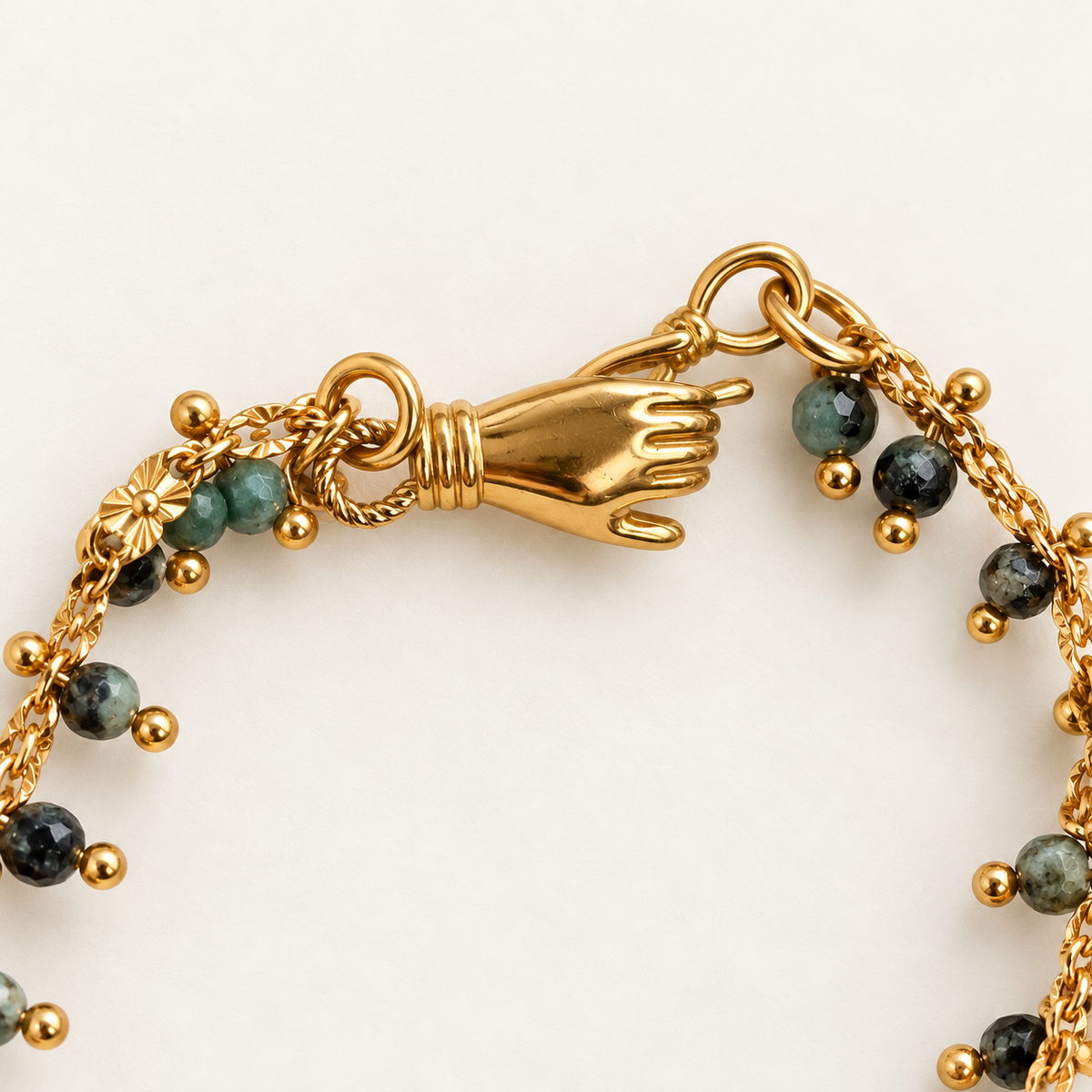 Gold-tone chain bracelet featuring a sculpted hand clasp and small round beads in dark green and black with gold spacer balls, shown on a plain light background.
