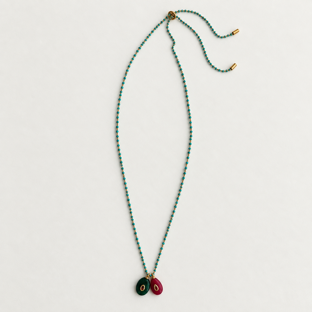 A long beaded necklace with small turquoise-blue and green beads, gold-toned hardware, and two oval pendant charms in dark green and burgundy with gold centers, laid flat on a light gray background.