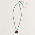 A long beaded necklace with small turquoise-blue and green beads, gold-toned hardware, and two oval pendant charms in dark green and burgundy with gold centers, laid flat on a light gray background.