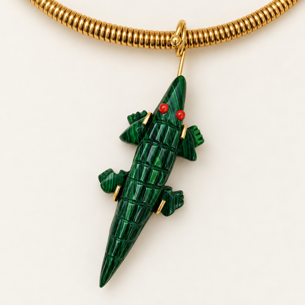 A green malachite crocodile pendant necklace with gold-tone metal accents and tiny red eyes, shown on a gold coiled chain against a clean off-white background.